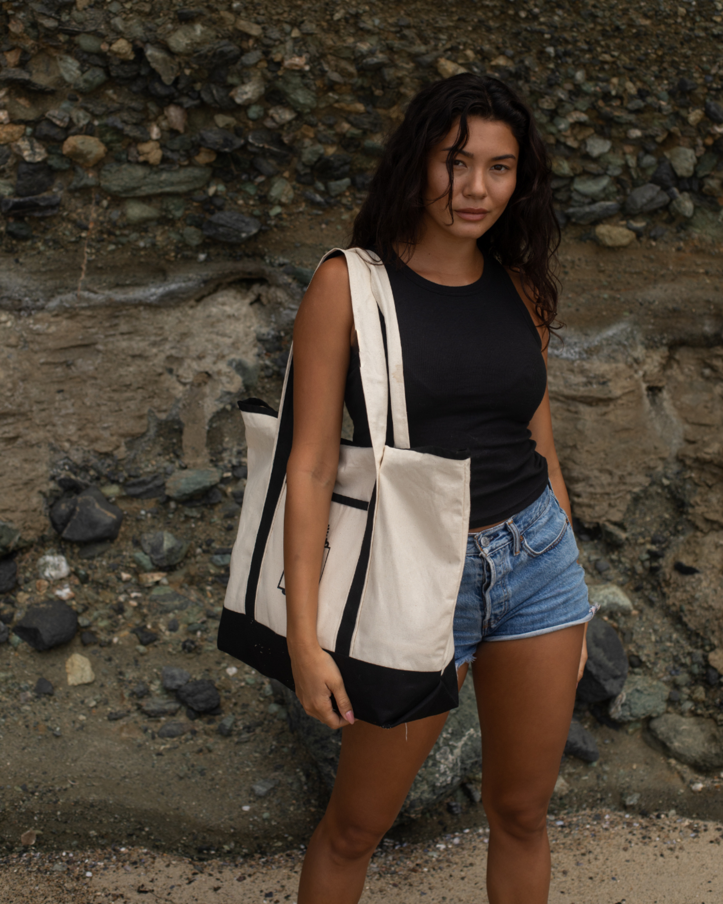 Woman holding a black and white tote bag with a logo against a rocky background