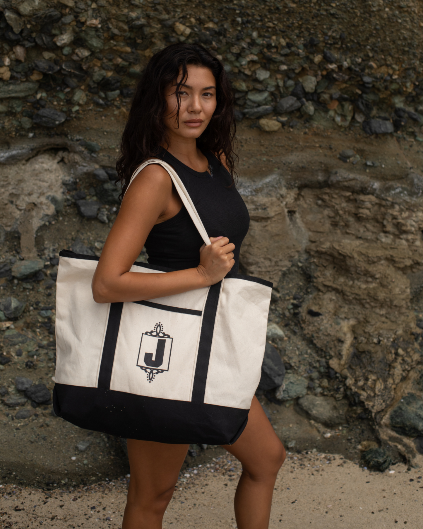 Woman holding a black and white tote bag with a logo against a rocky background