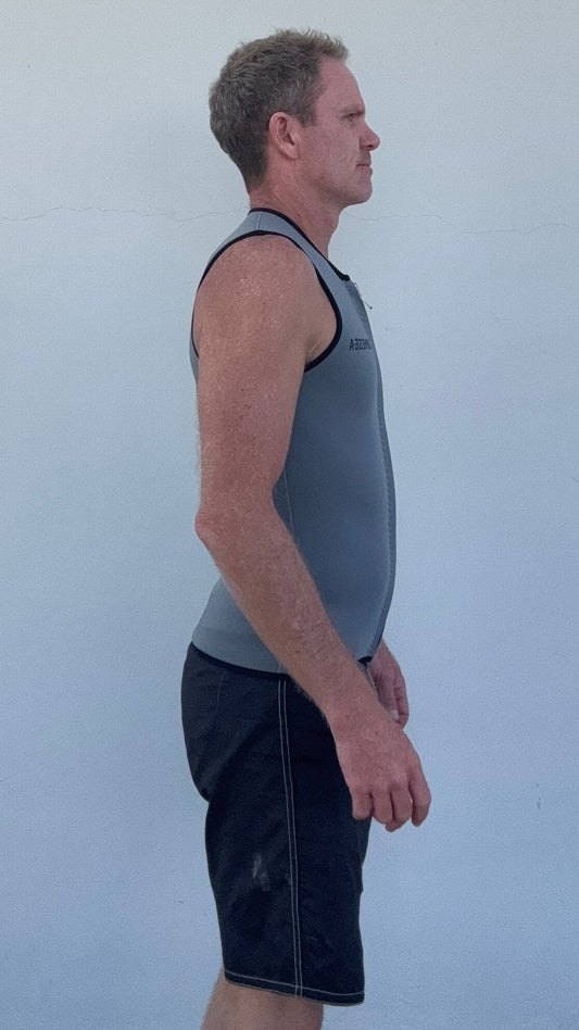 A man wearing a gray neoprene athletic vest with a front zipper and black trim, standing in profile against a plain white wall.