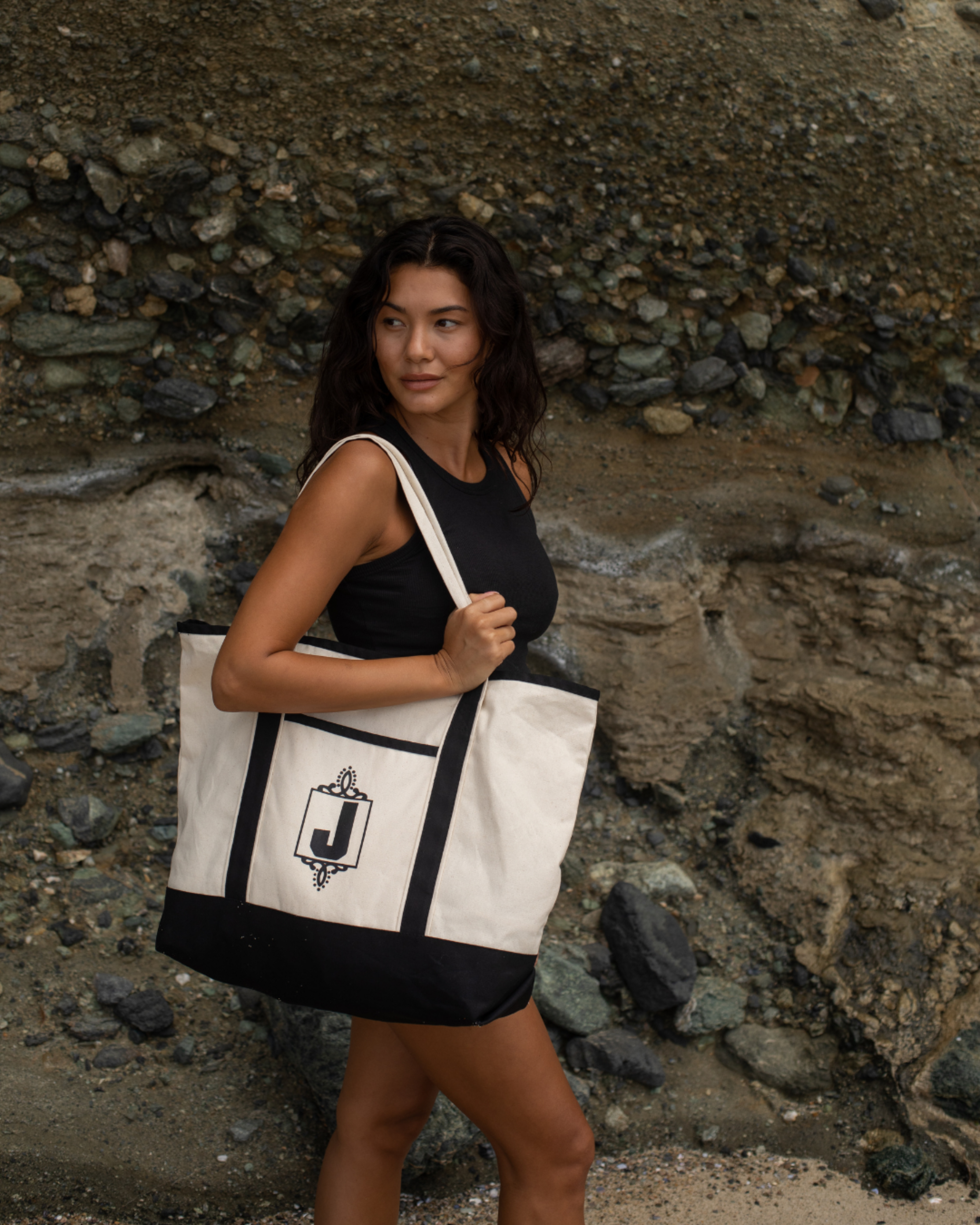 Woman holding a tote bag with a logo against a stone wall.