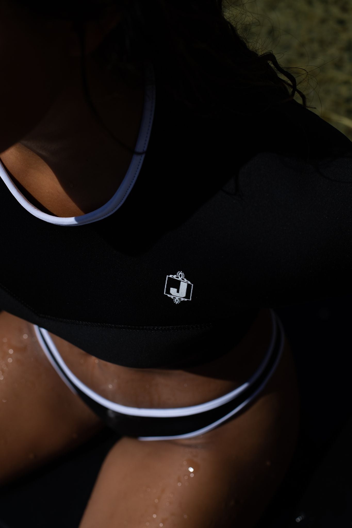Close-up of a Women wearing black Crop top and a bikini bottom shot from above with a white Jonesea Logo. 