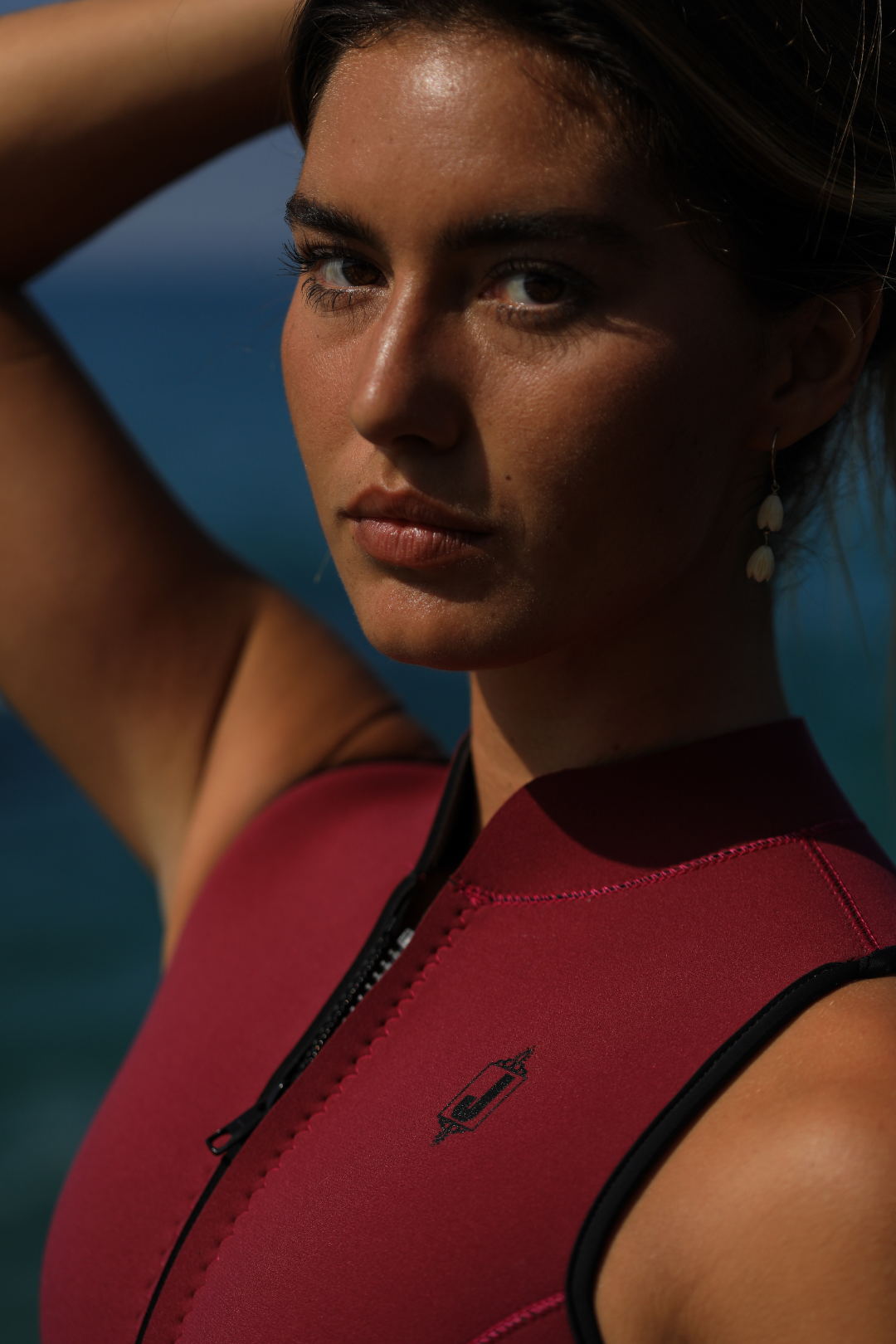 Jonesea Sangria High-Neck One-Piece Springsuit – Close-up of handmade women's neoprene wetsuit in Sangria, front zip detail, ocean background