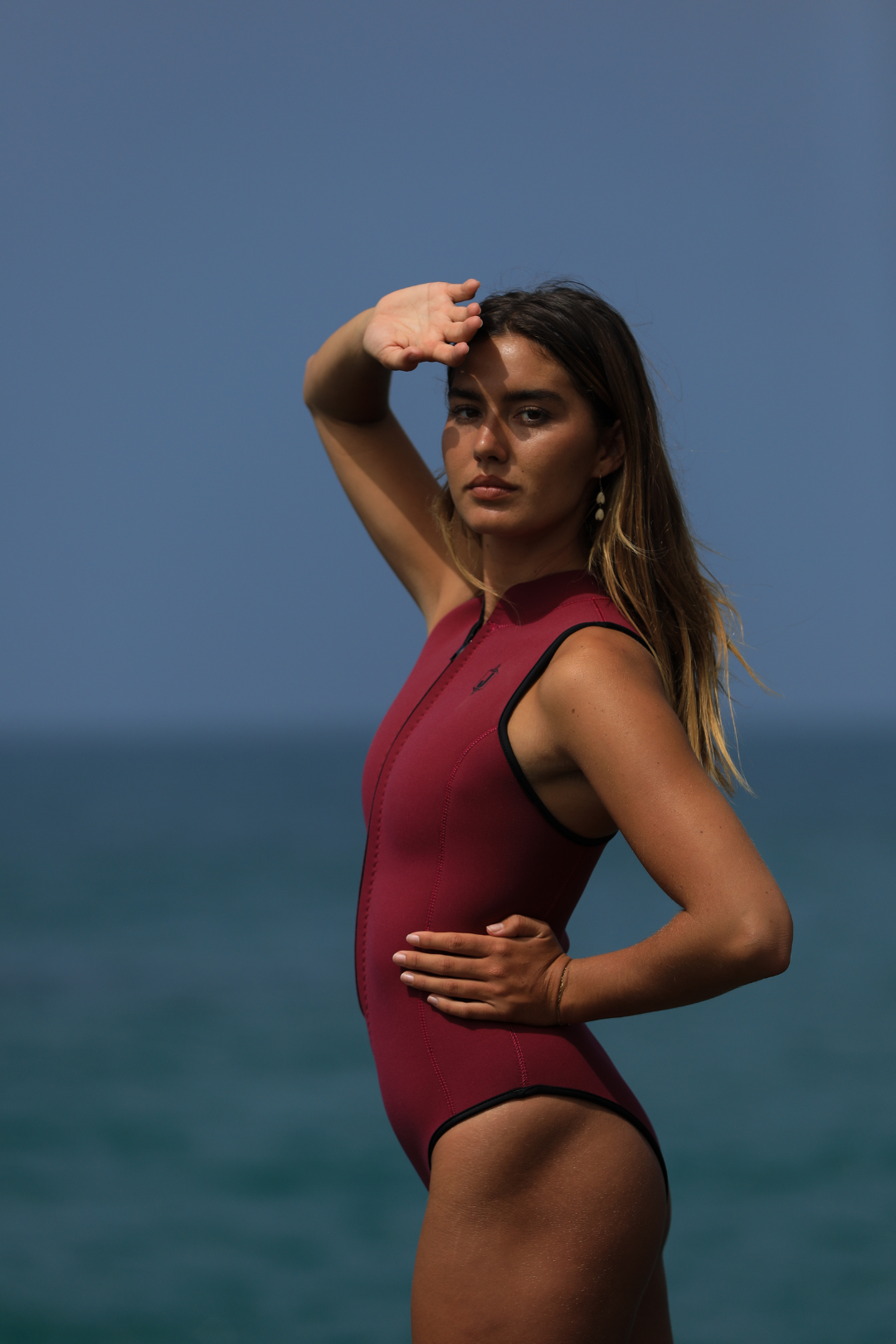 Jonesea Sangria High-Neck One-Piece Springsuit – Front view of handmade women's neoprene wetsuit in Sangria, open zip, ocean background