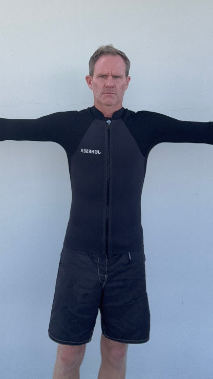 Man wearing the Men’s Graphite Surf Jacket in Graphite with arms outstretched against a plain light gray wall.